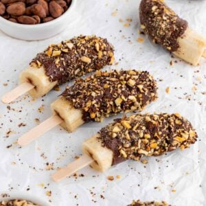 chocolate covered frozen bananas on popsicle sticks with crushed nuts