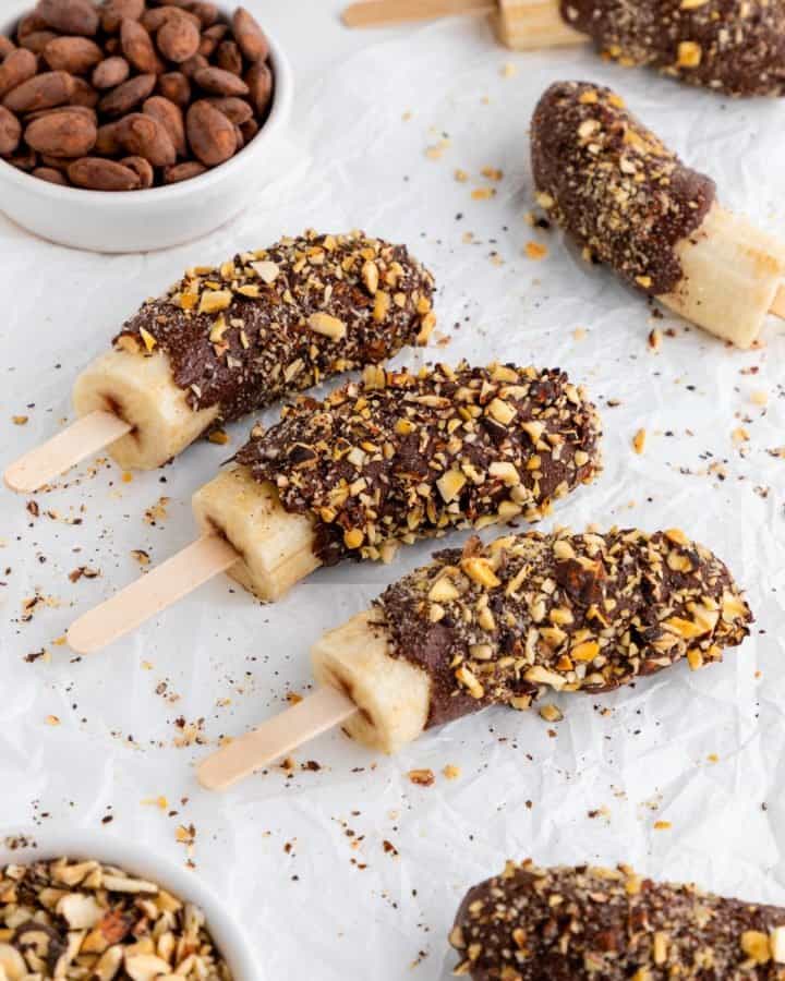 chocolate covered frozen bananas on popsicle sticks with crushed nuts