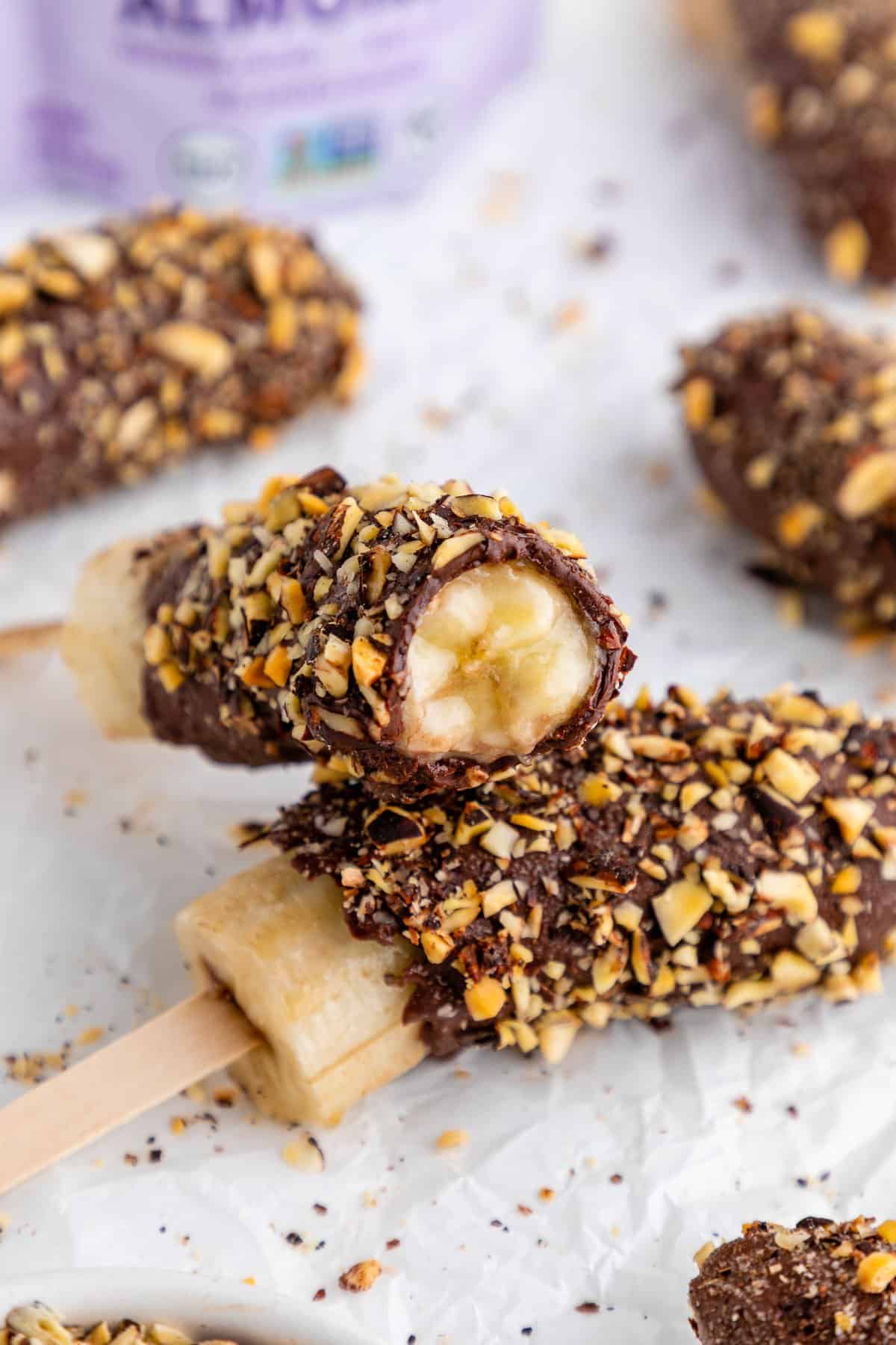 a half bitten chocolate covered frozen banana pop covered in crushed nuts