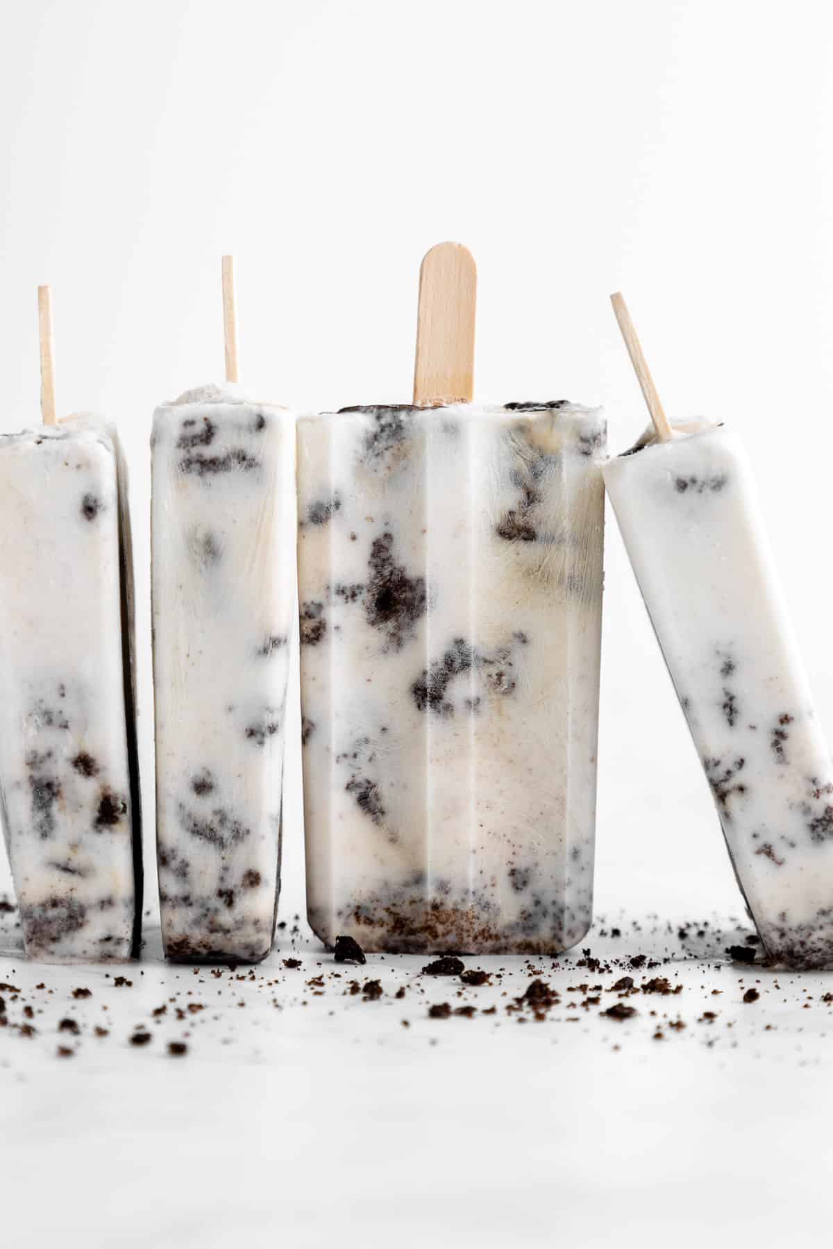 four vegan cookies and cream popsicles with crushed Oreos standing upside down