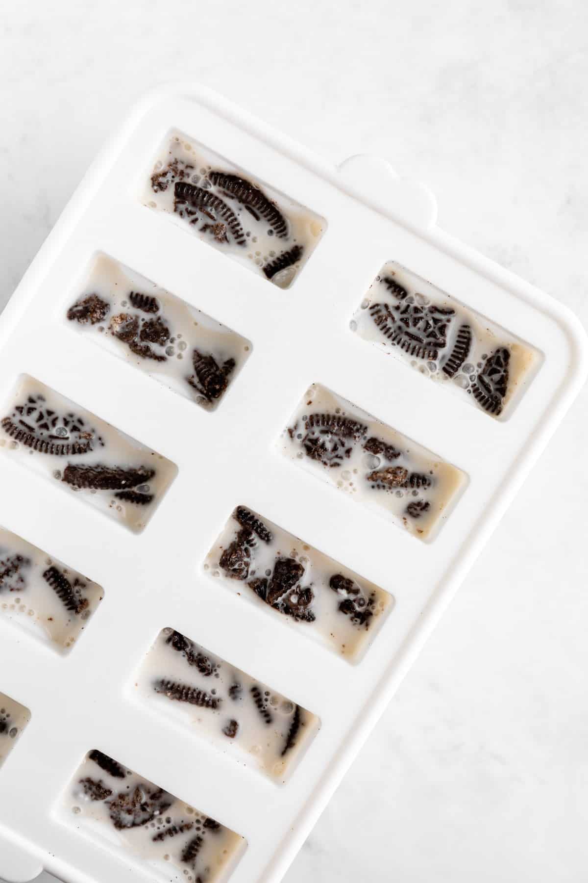 a white popsicle mold filled with coconut milk and crushed Oreos