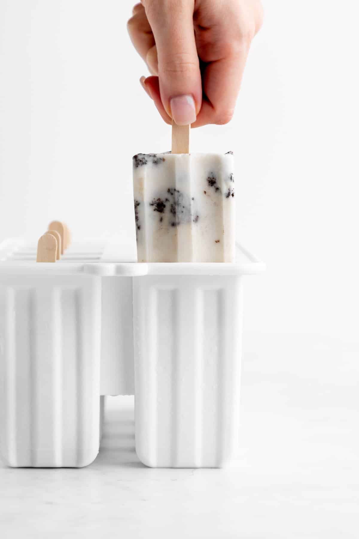 a hand pulling a cookies and cream popsicle out of a white popsicle mold