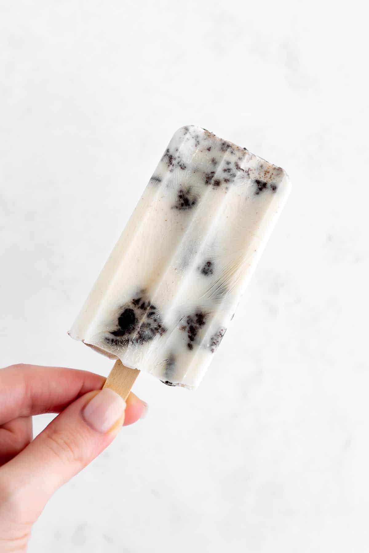 a hand holding a vegan cookies and cream popsicle