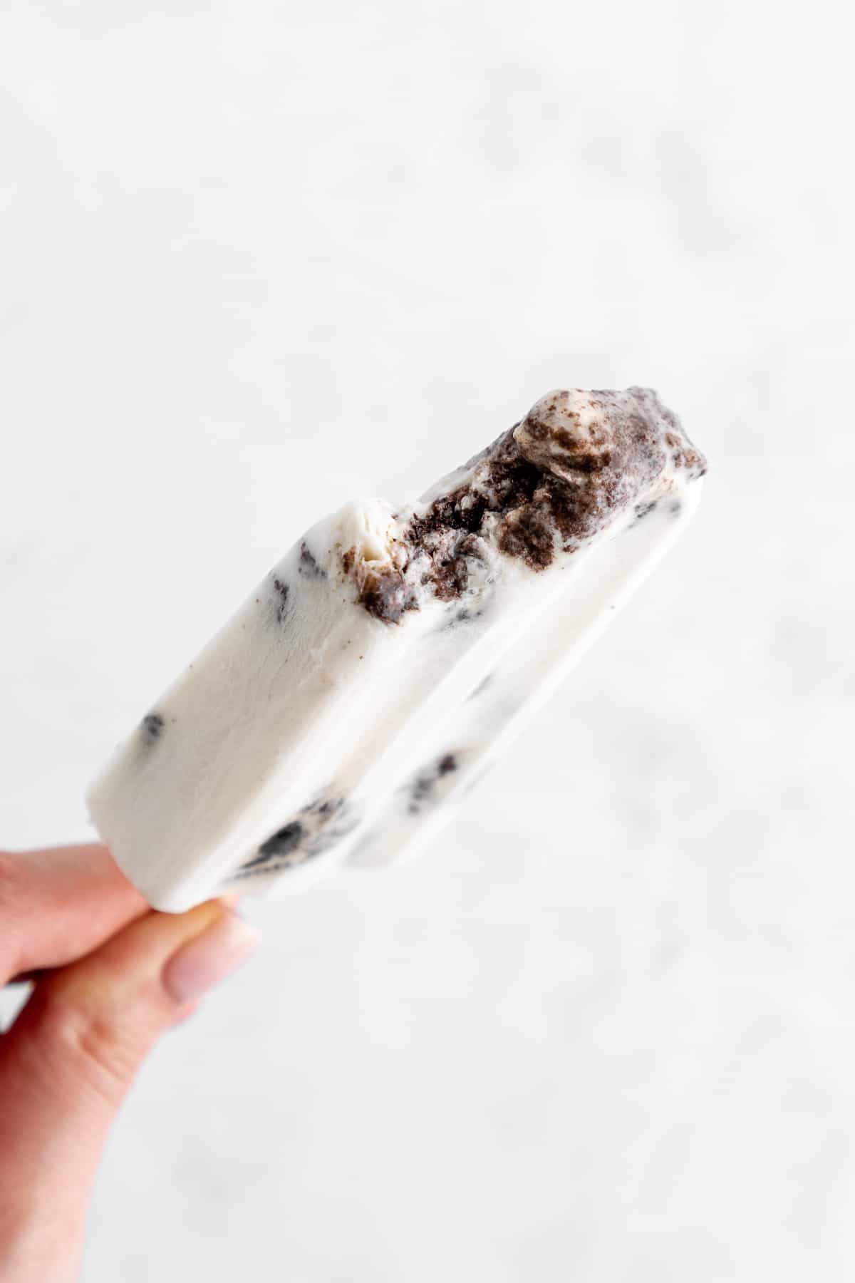 a hand holding a partially bitten vegan cookies and cream popsicle