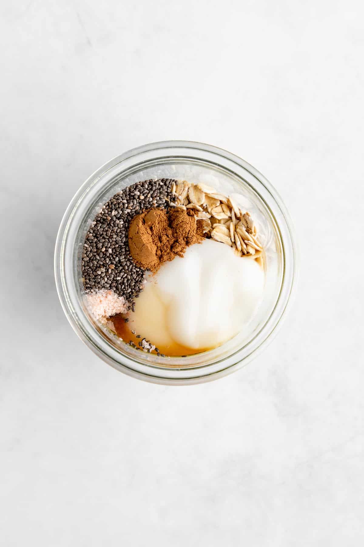 overhead photo of rolled oats, yogurt, chia seeds, and cinnamon in a jar