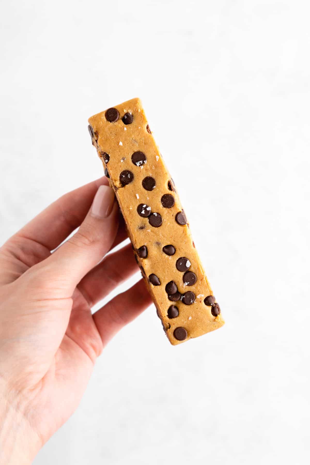 a hand holding a homemade vegan cookie dough protein bar with chocolate chips