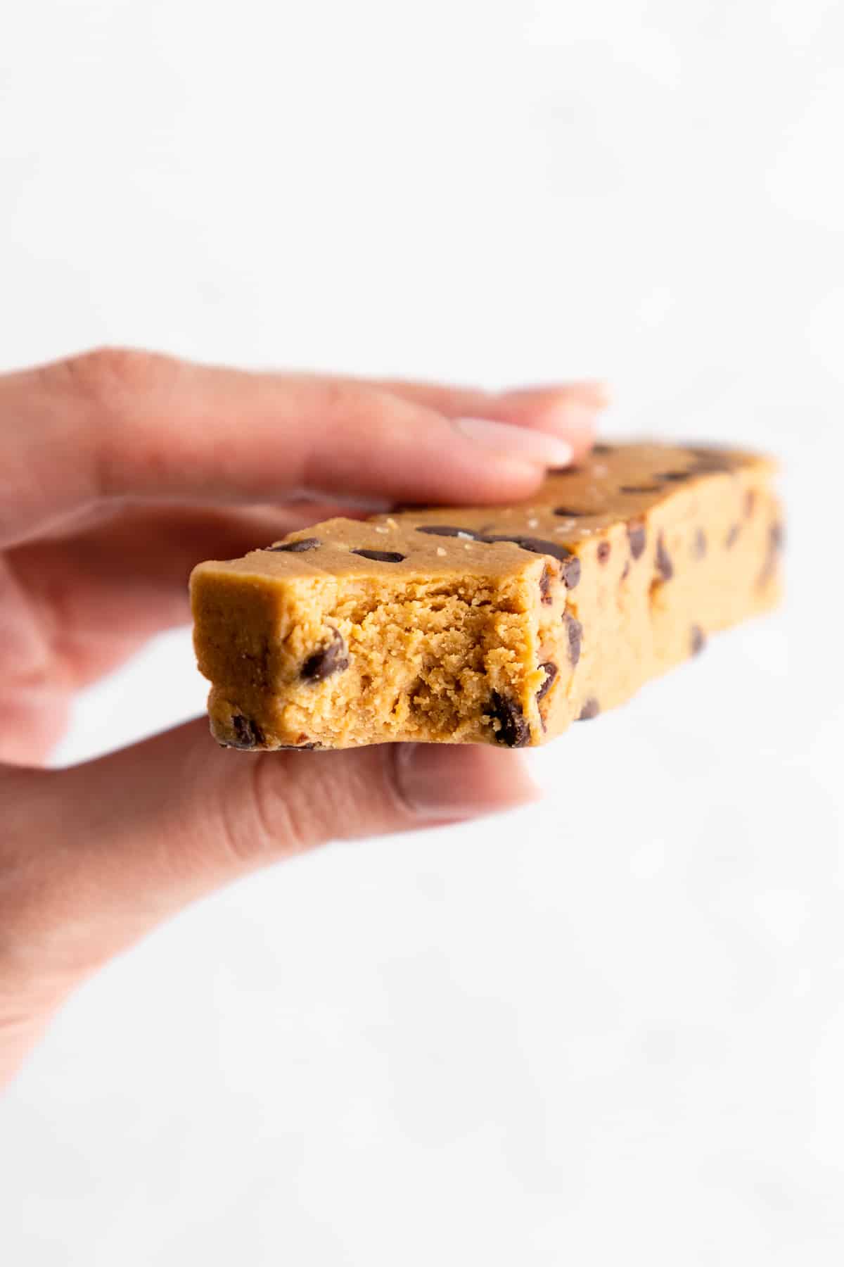 a hand holding a bitten chocolate chip cookie dough protein bar