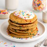 a stack of healthy funfetti pancakes with frosting and sprinkles on a white plate