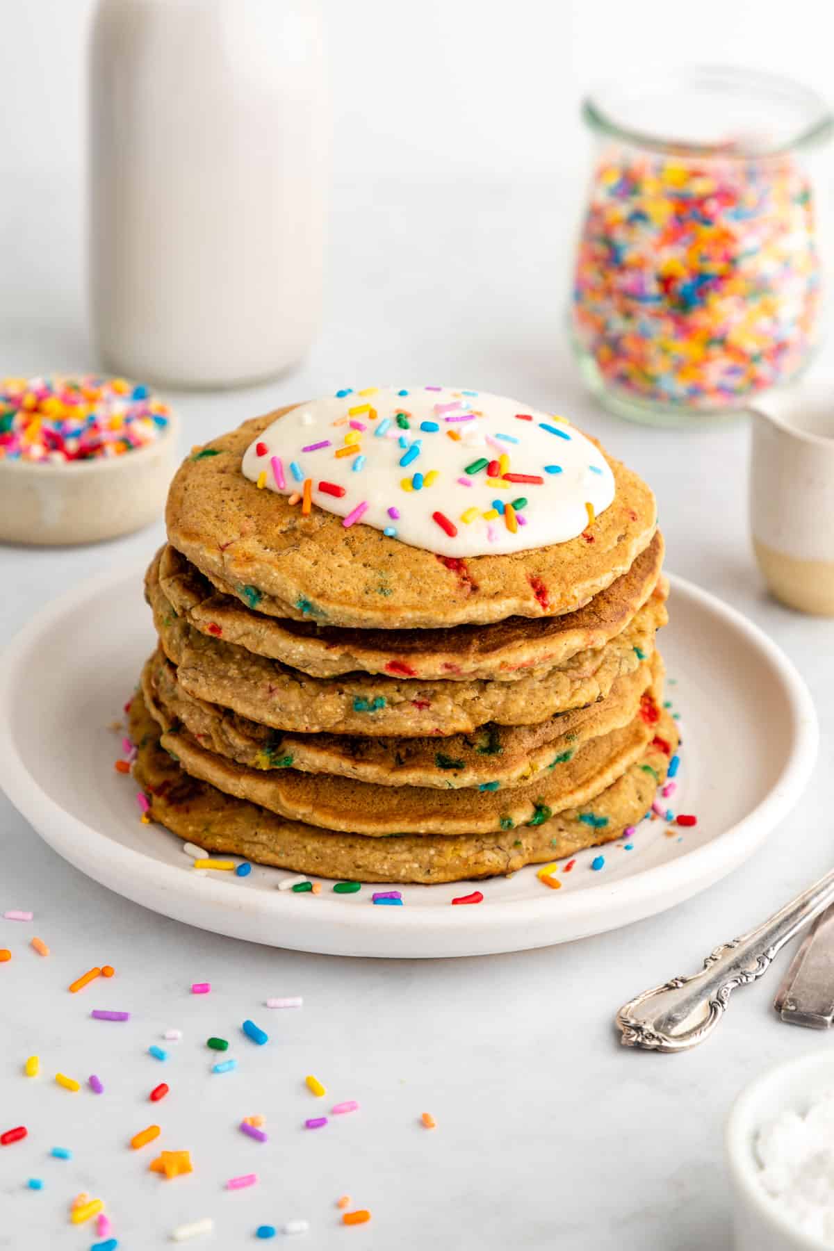 a stack of healthy funfetti pancakes with frosting and sprinkles on a white plate