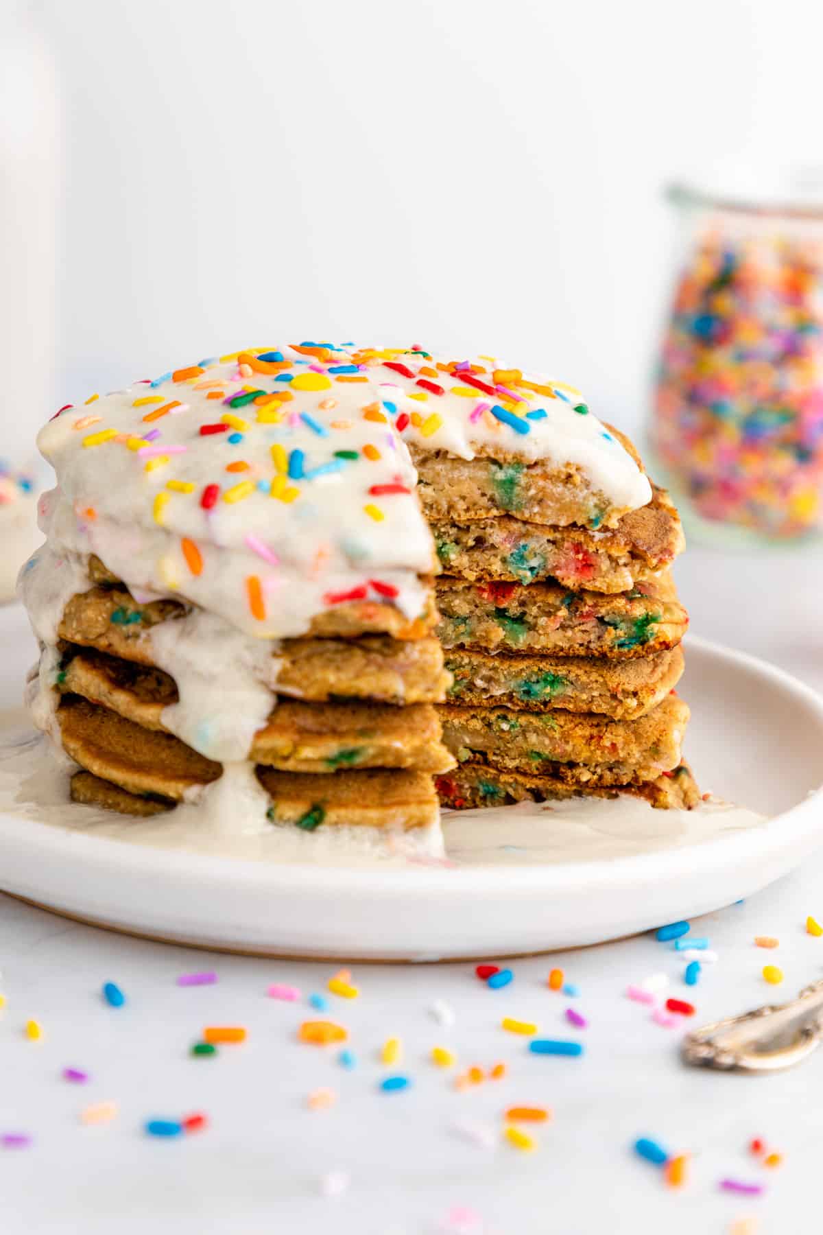 a sliced stack of healthy funfetti pancakes with frosting and sprinkles on top