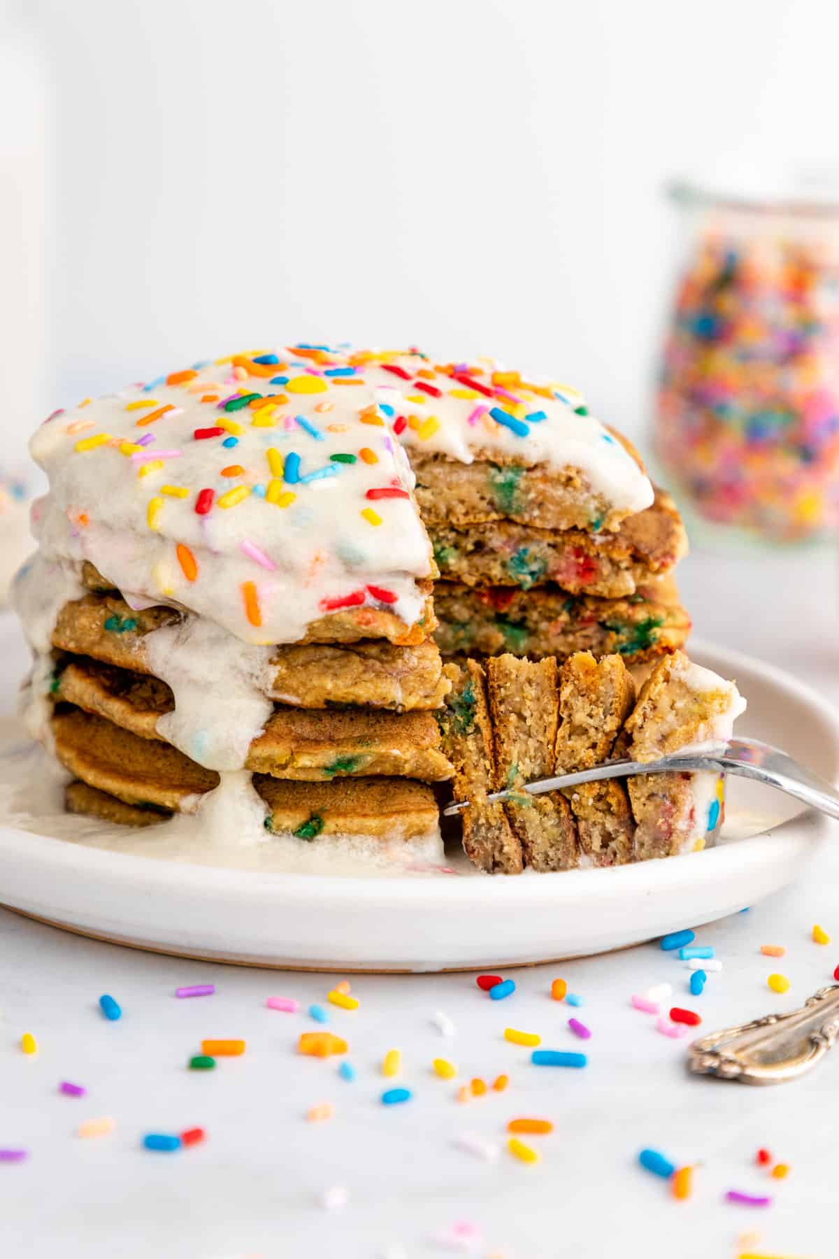 a fork digging into a stack of healthy funfetti pancakes with icing and sprinkles