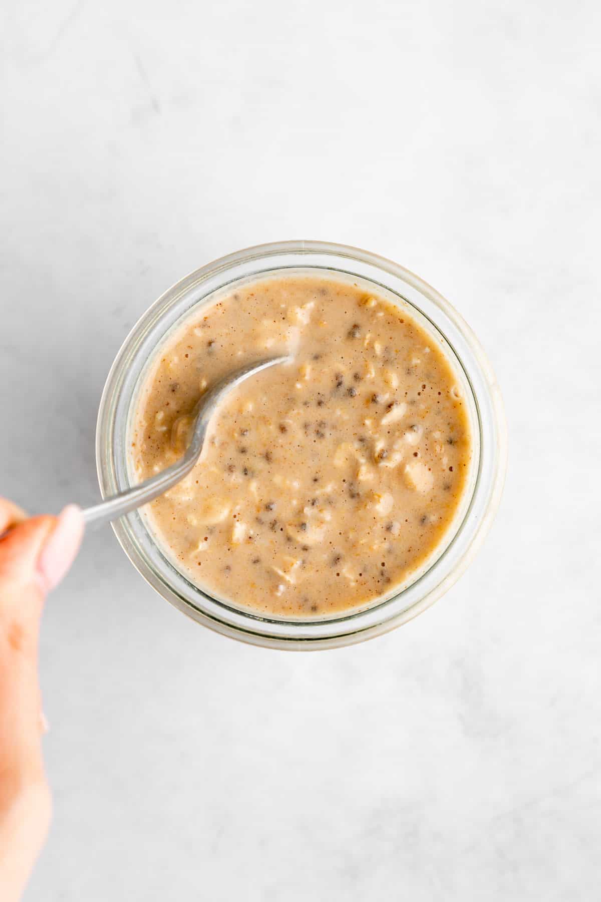 left hand holding a spoon mixing peanut butter overnight oats in a jar