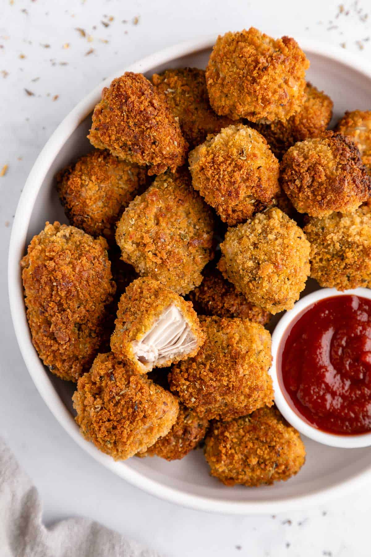 crispy vegan jackfruit nuggets on a white plate with a bite taken out of one of the nuggets