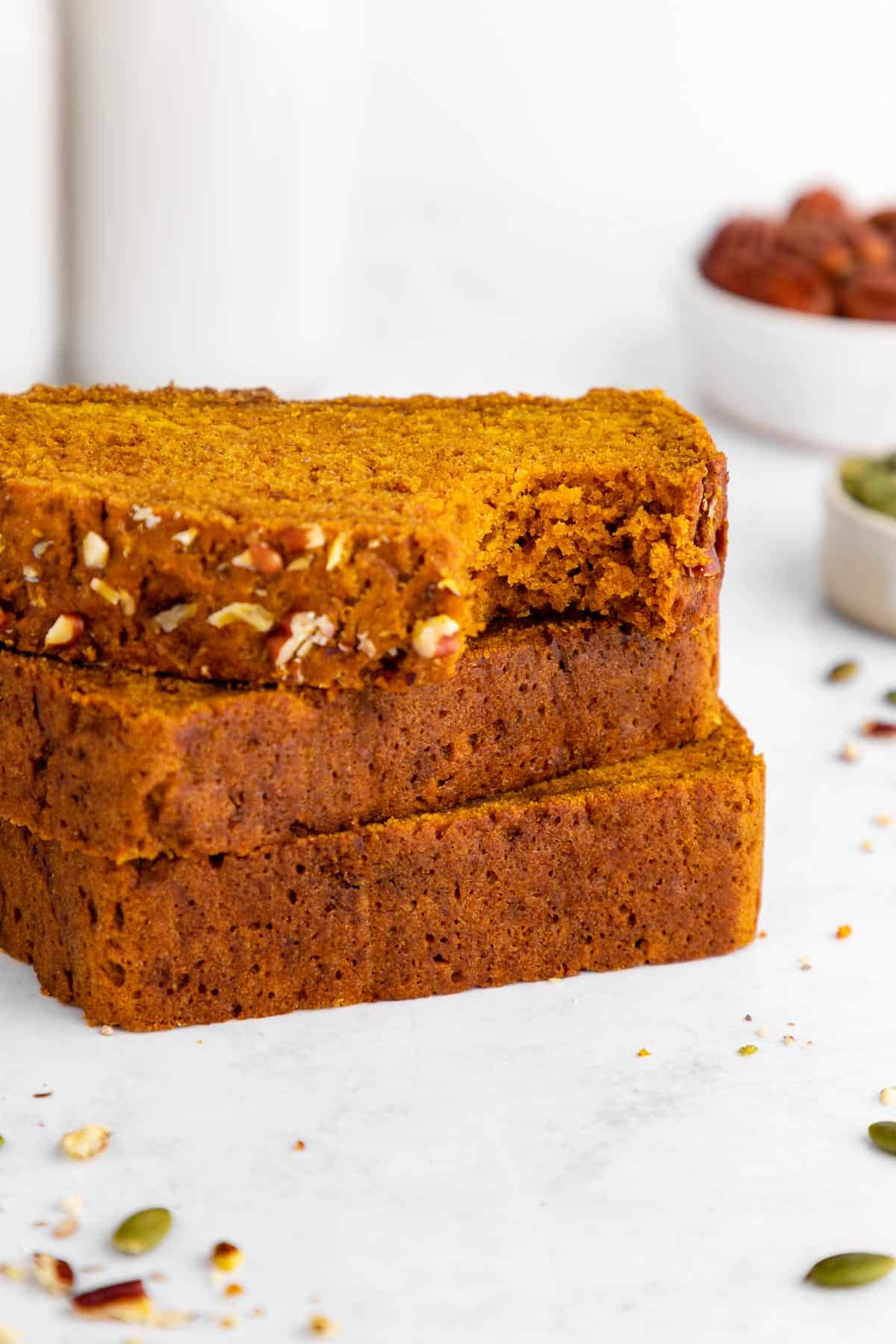 a stack of three slices of vegan pumpkin bread with a bite taken out of the top slice