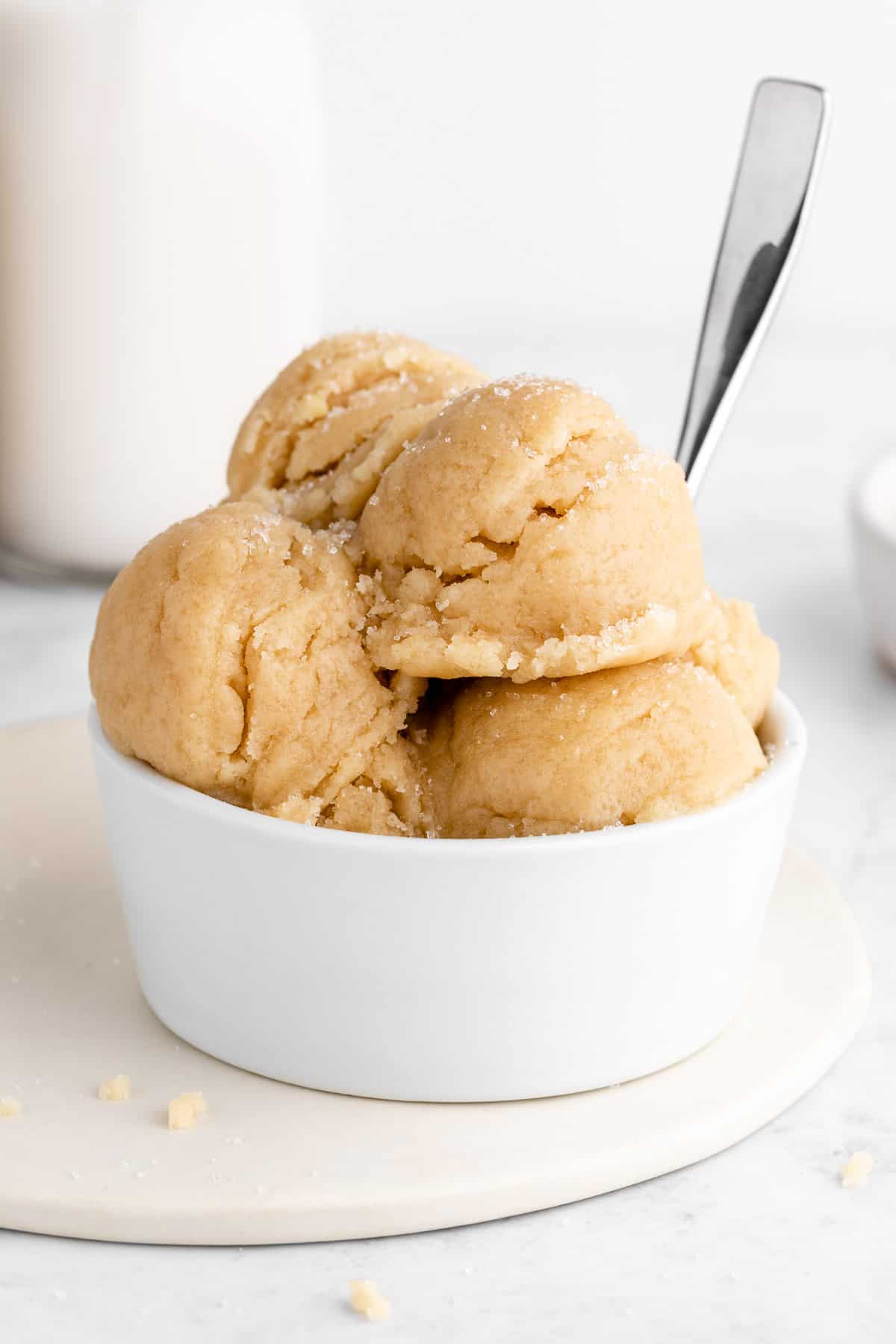 vegan edible sugar cookie dough scoops stacked in a white bowl with a spoon sticking out of it