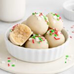 a bowl of Christmas sugar cookie truffles with a bite taken out of one