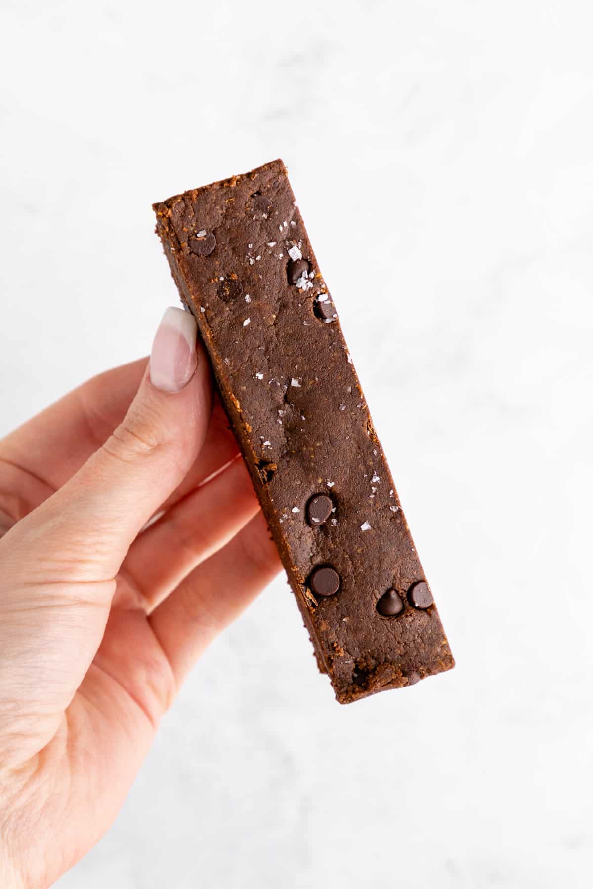 a hand holding a homemade chocolate brownie protein bar