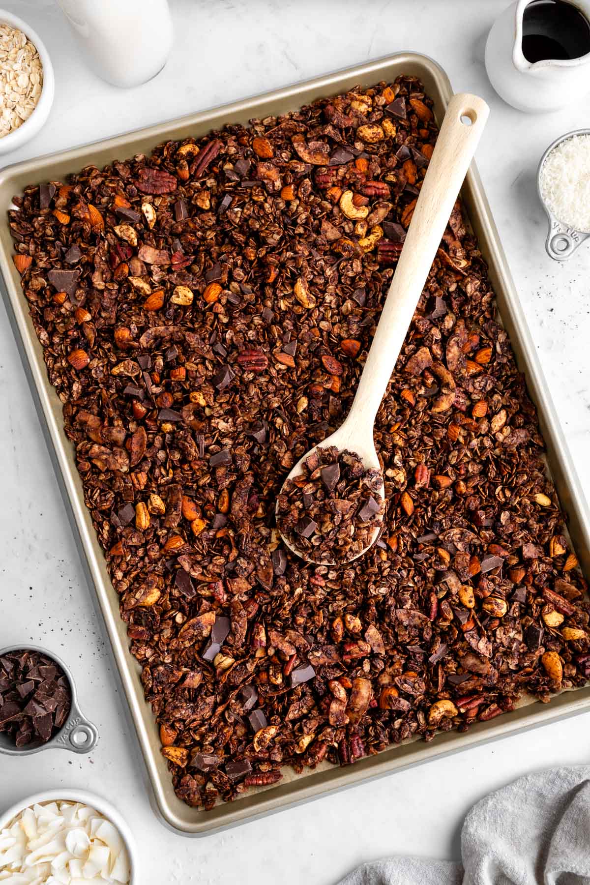 homemade chocolate coconut granola spread on a baking sheet with a wooden spoon