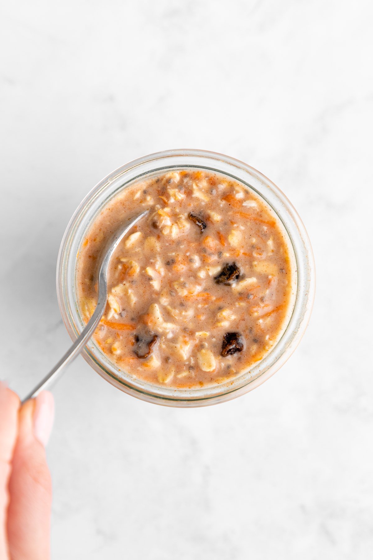 a hand holding a spoon mixing carrot cake overnight oats in a jar