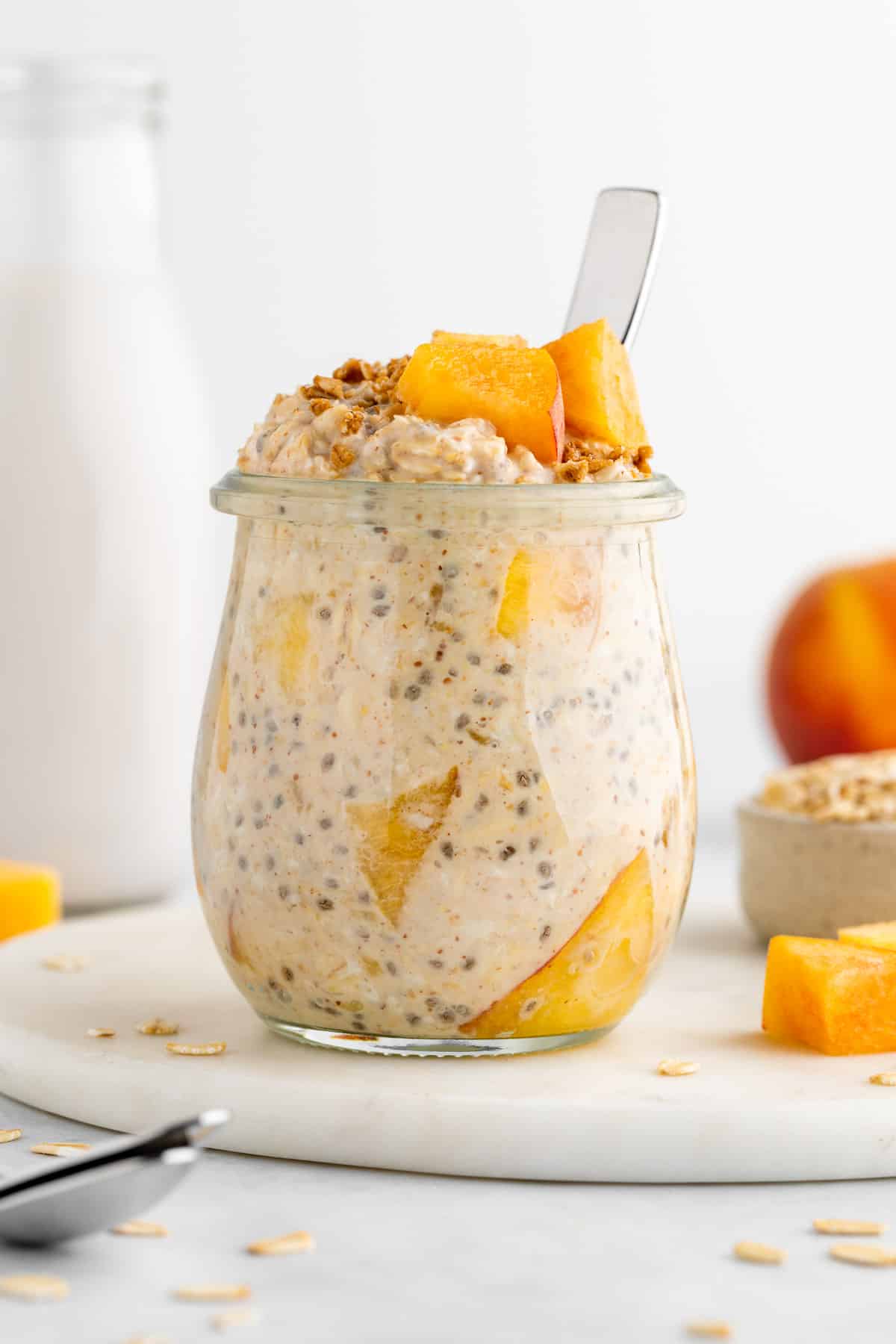 a jar of peaches and cream overnight oats with a spoon inside it