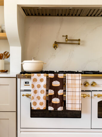 a chocolate chip cookie towel, cinnamon roll towel, and a plaid towel hanging over an oven handle