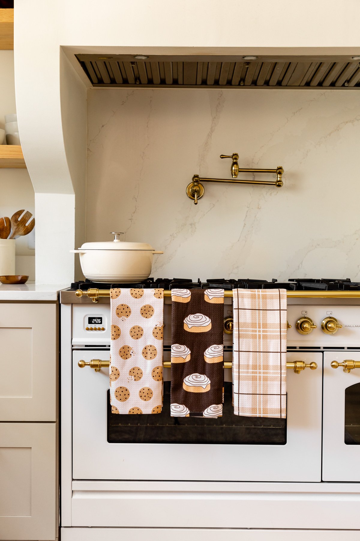 a chocolate chip cookie towel, cinnamon roll towel, and a plaid towel hanging over an oven handle