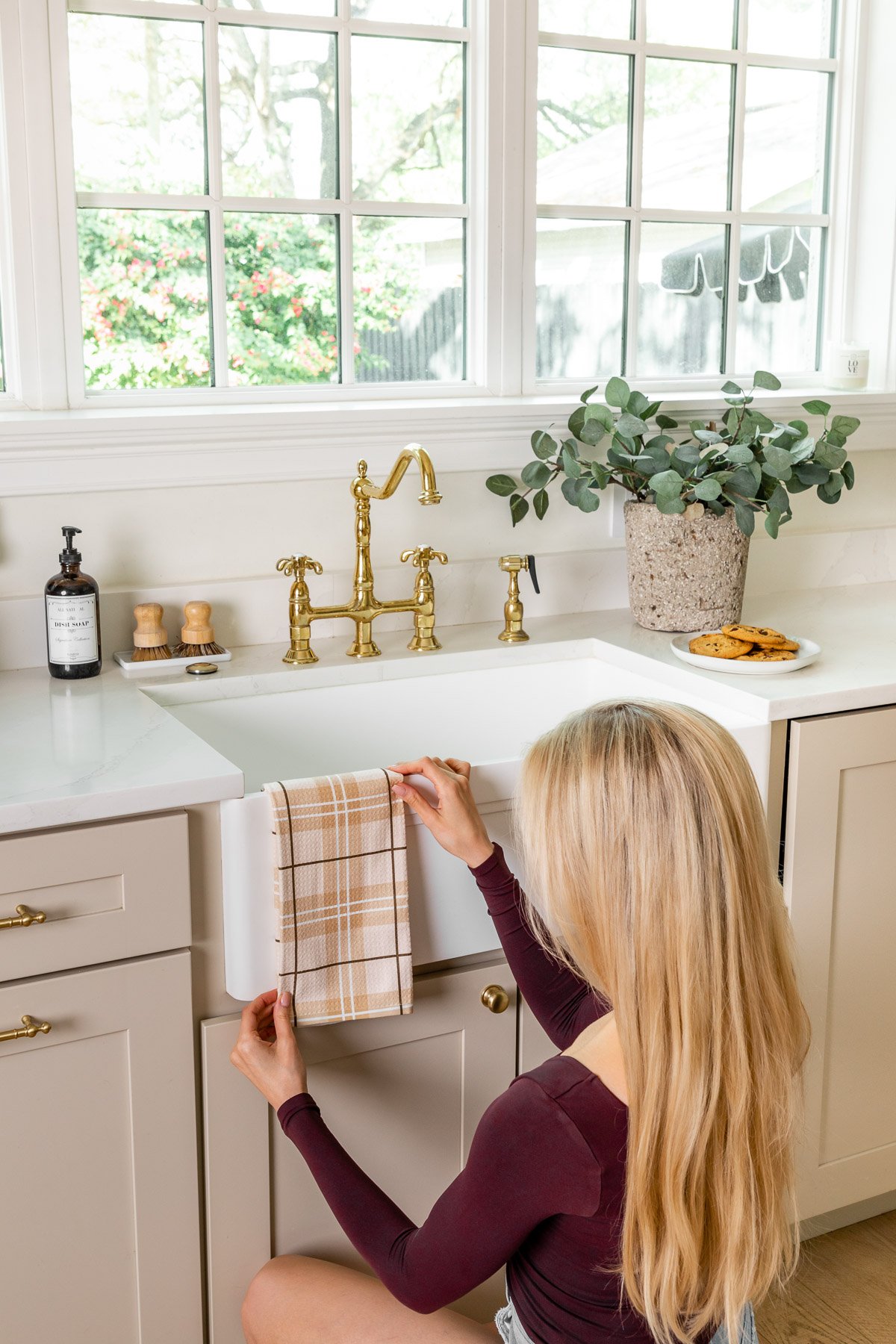 a blonde girl hanging a plaid kitchen tea towel over a farmhouse sink