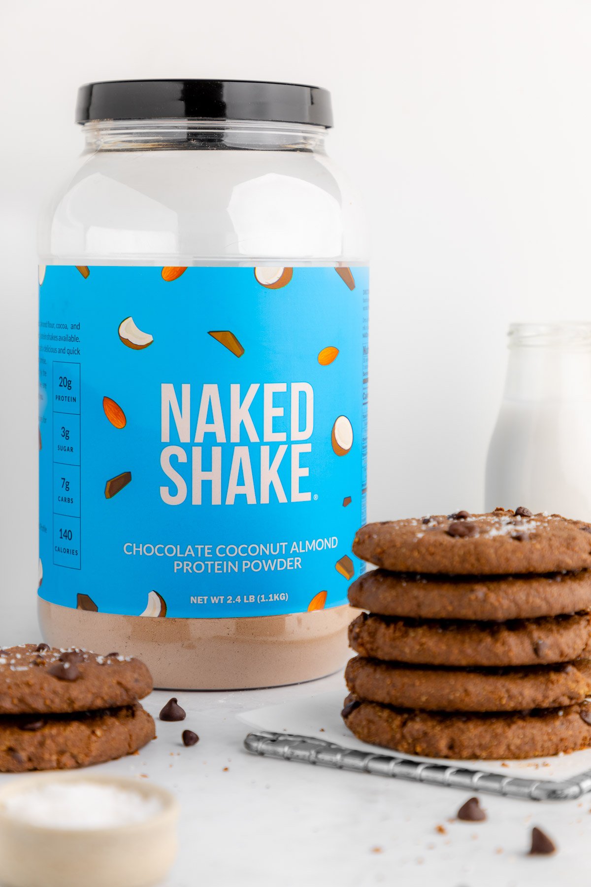 Naked Nutrition chocolate coconut almond protein powder beside a stack of vegan protein cookies