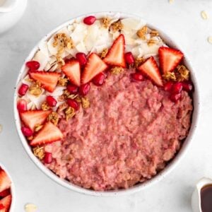 vegan strawberry oatmeal inside a ceramic bowl with granola and coconut flakes on top