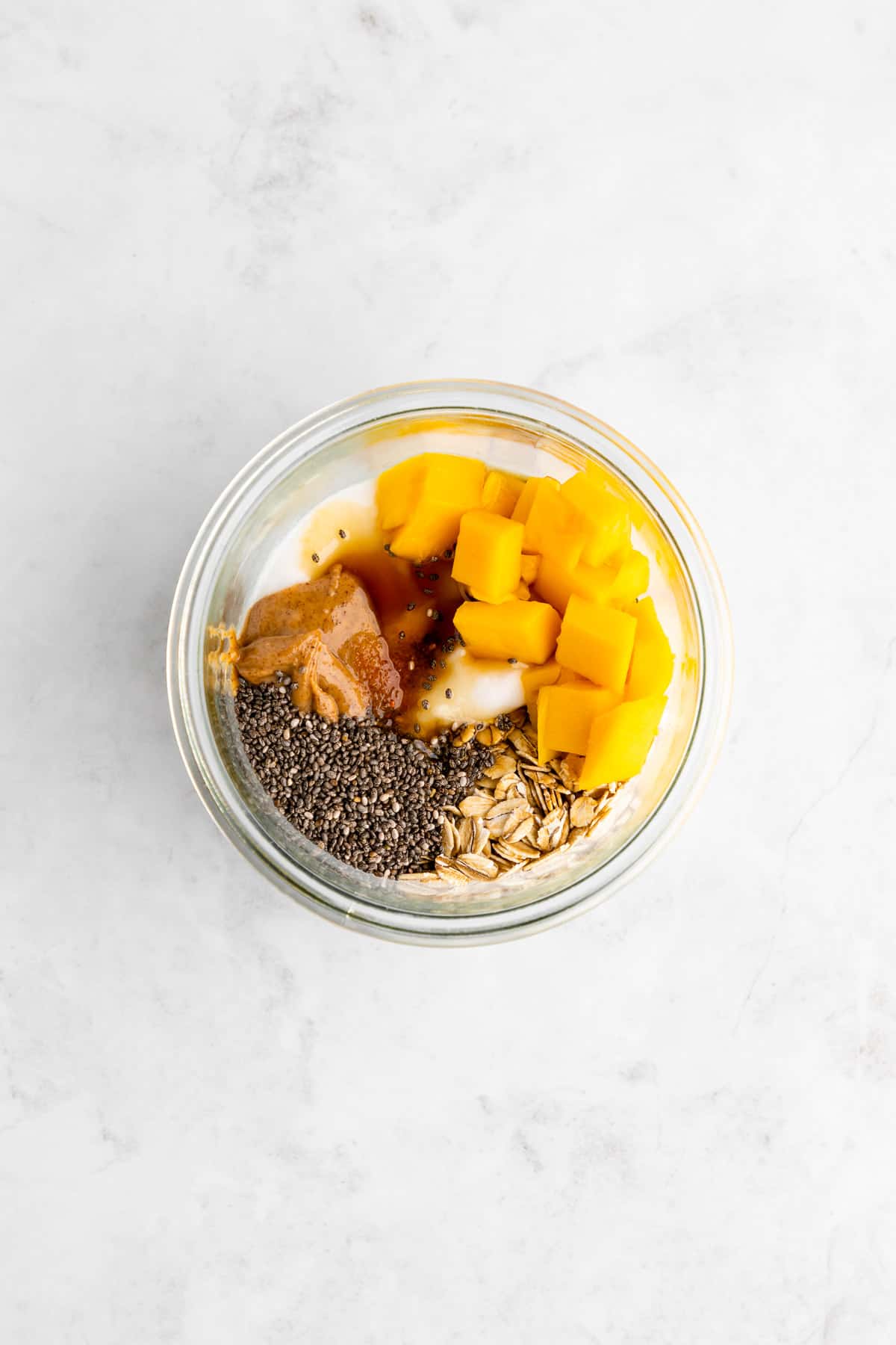 rolled oats, mango, yogurt, chia seeds, maple syrup, and cinnamon inside a glass mason jar