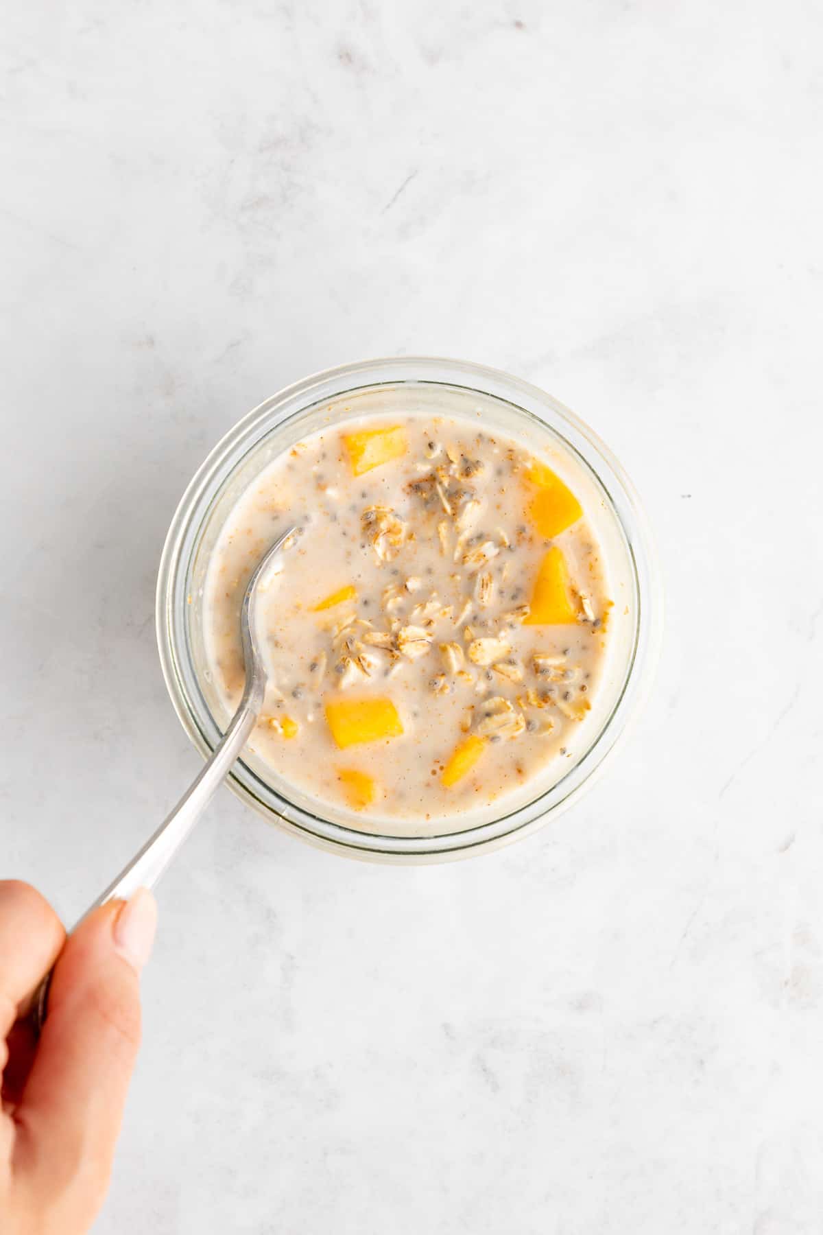 mixing mango overnight oats inside a glass mason jar