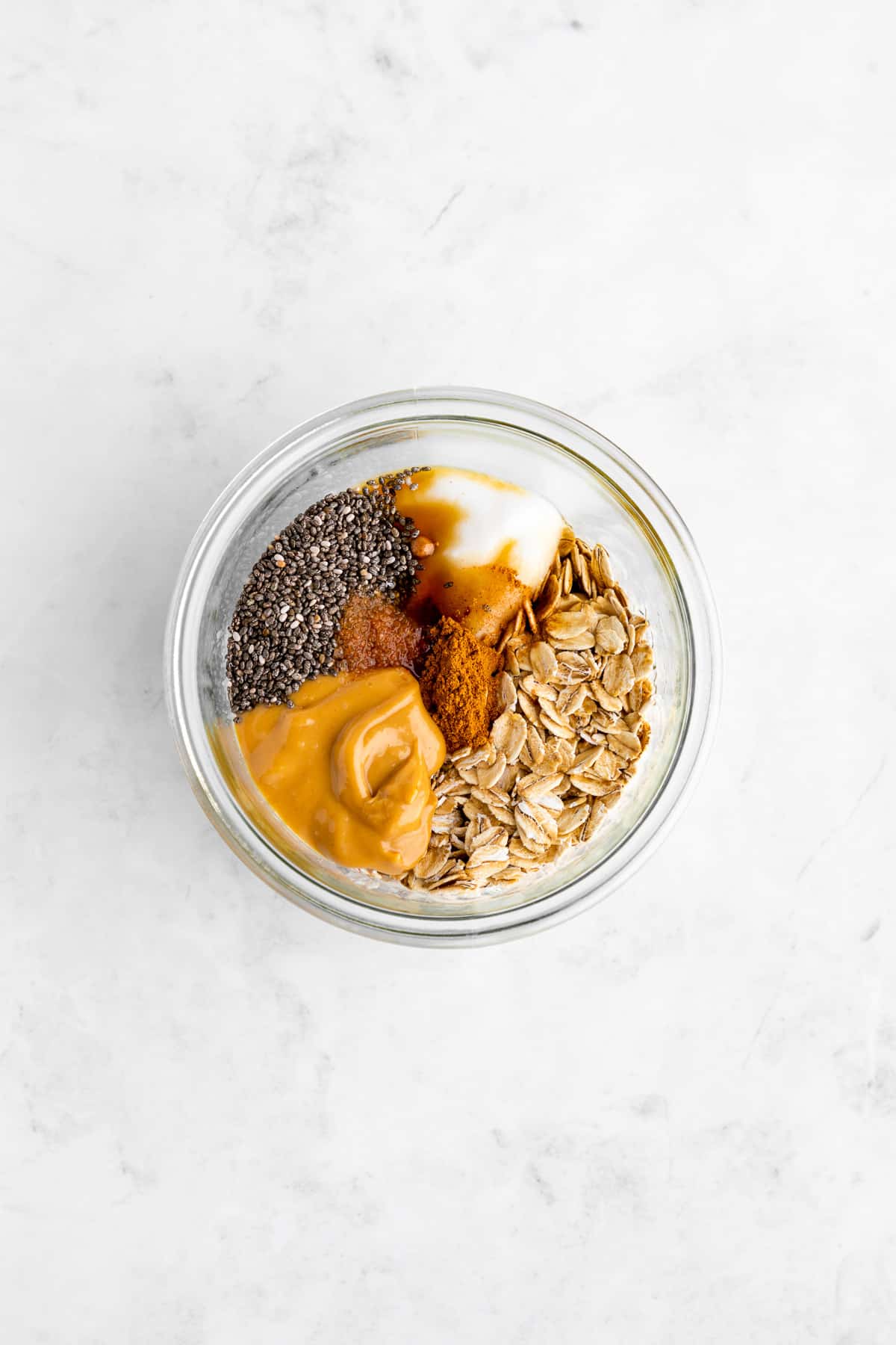 rolled oats, peanut butter, yogurt, chia seeds, maple syrup, and cinnamon inside a glass mason jar