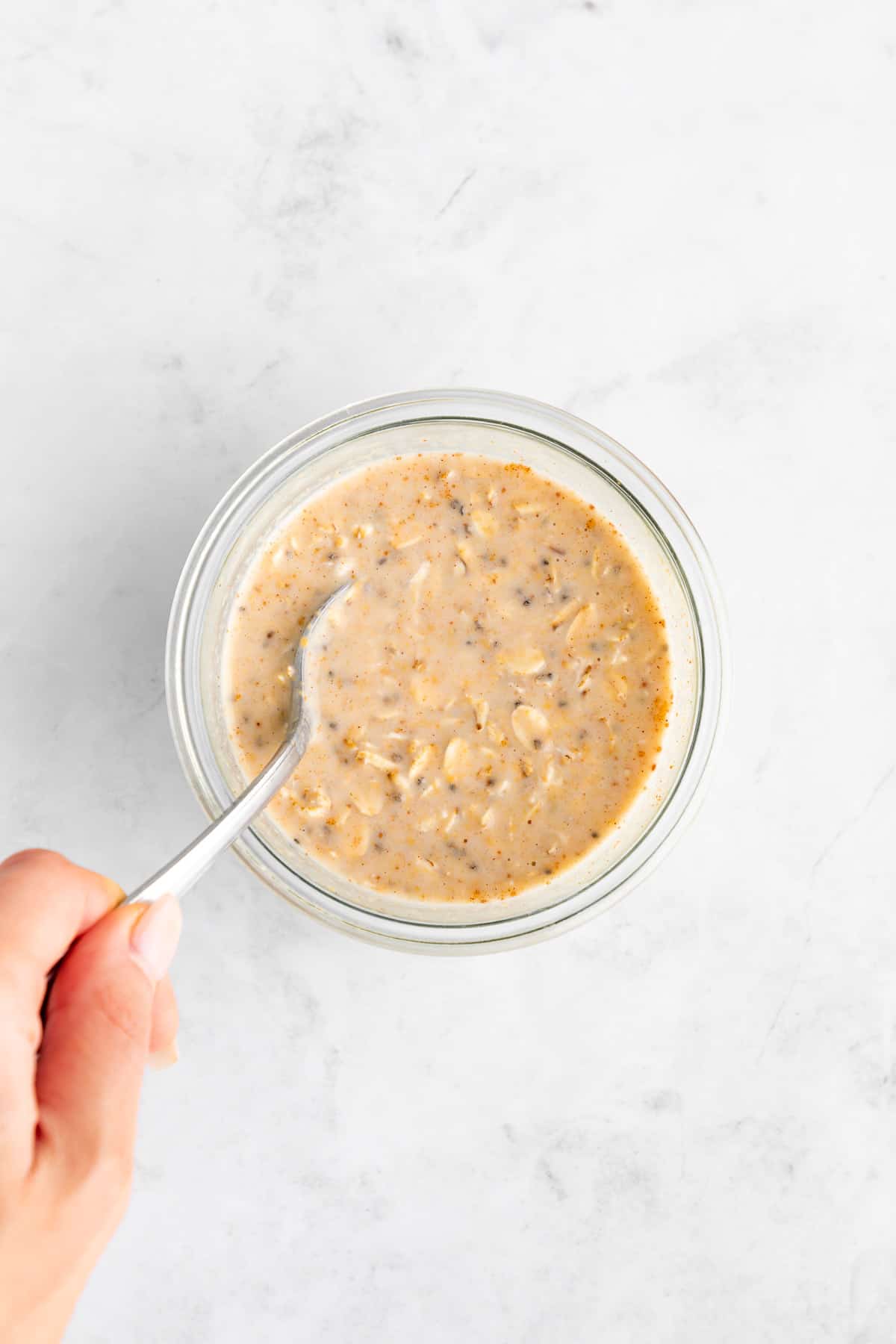mixing peanut butter and jelly overnight oats inside a glass mason jar