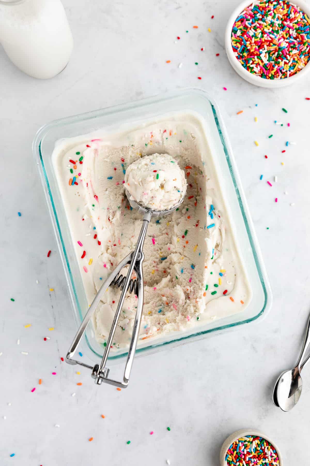 an ice scream scoop scooping vegan cake batter ice cream out of a glass container