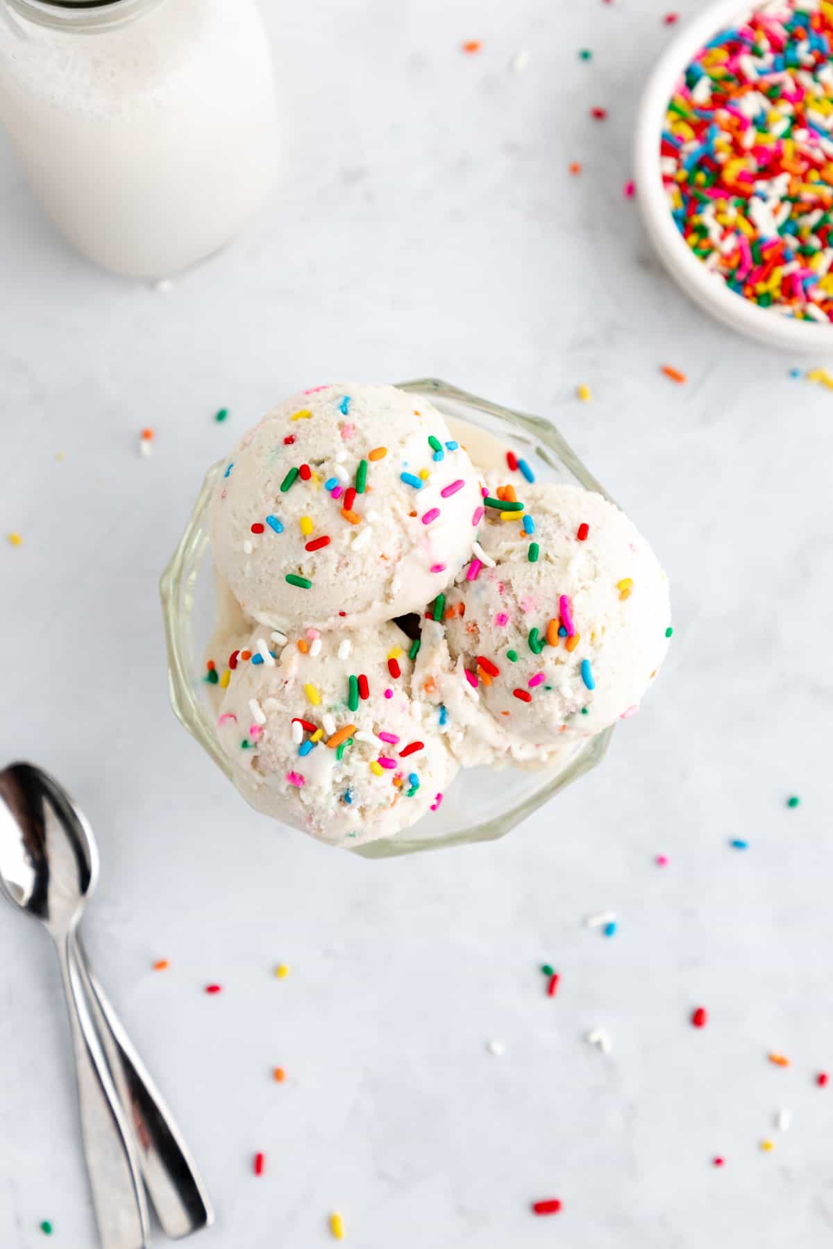 scoops of vegan cake batter ice cream inside a sundae glass with rainbow sprinkles