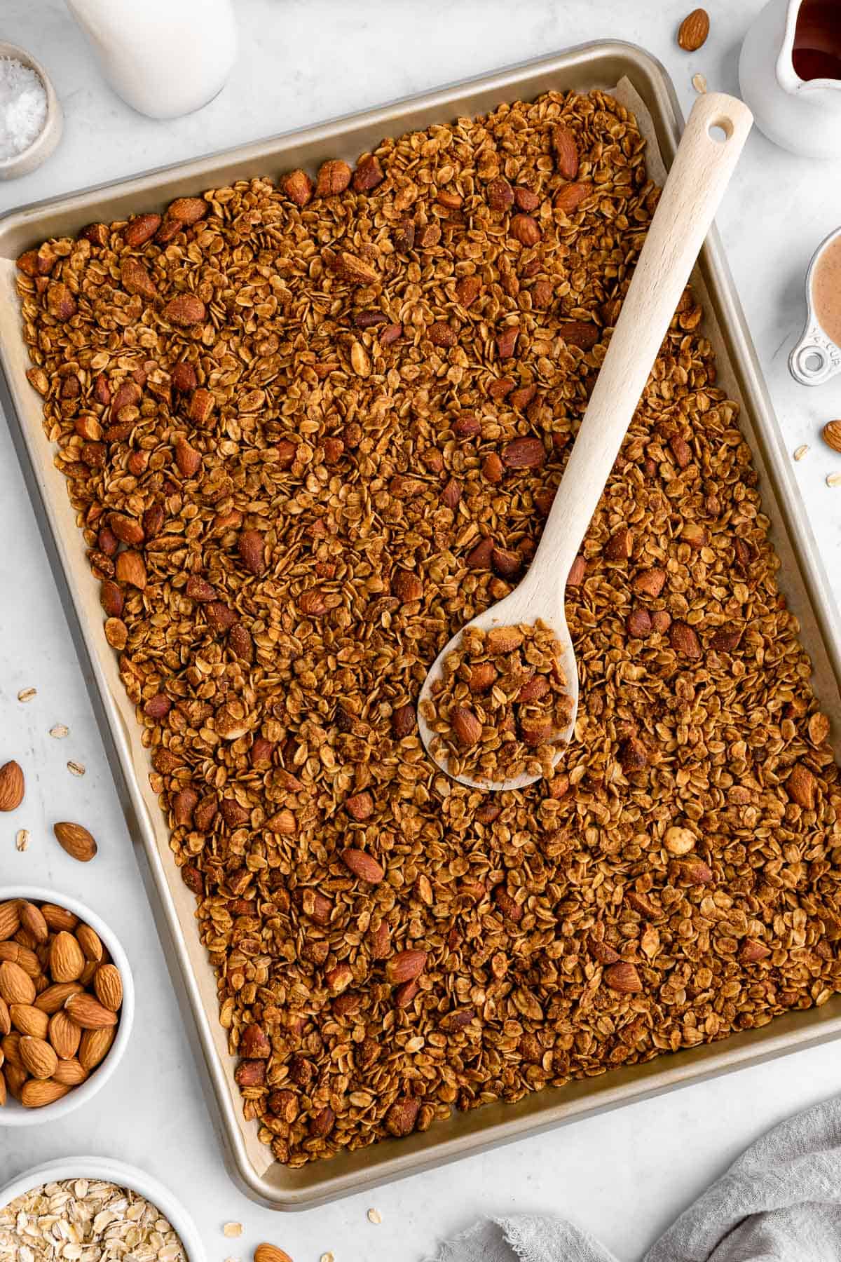 homemade almond butter granola on a baking sheet with a wooden spoon