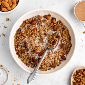 a bowl of homemade almond butter granola with almond milk and a spoon