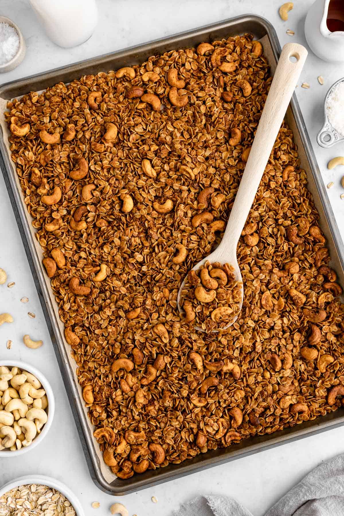homemade cashew butter granola on a baking sheet with a wooden spoon