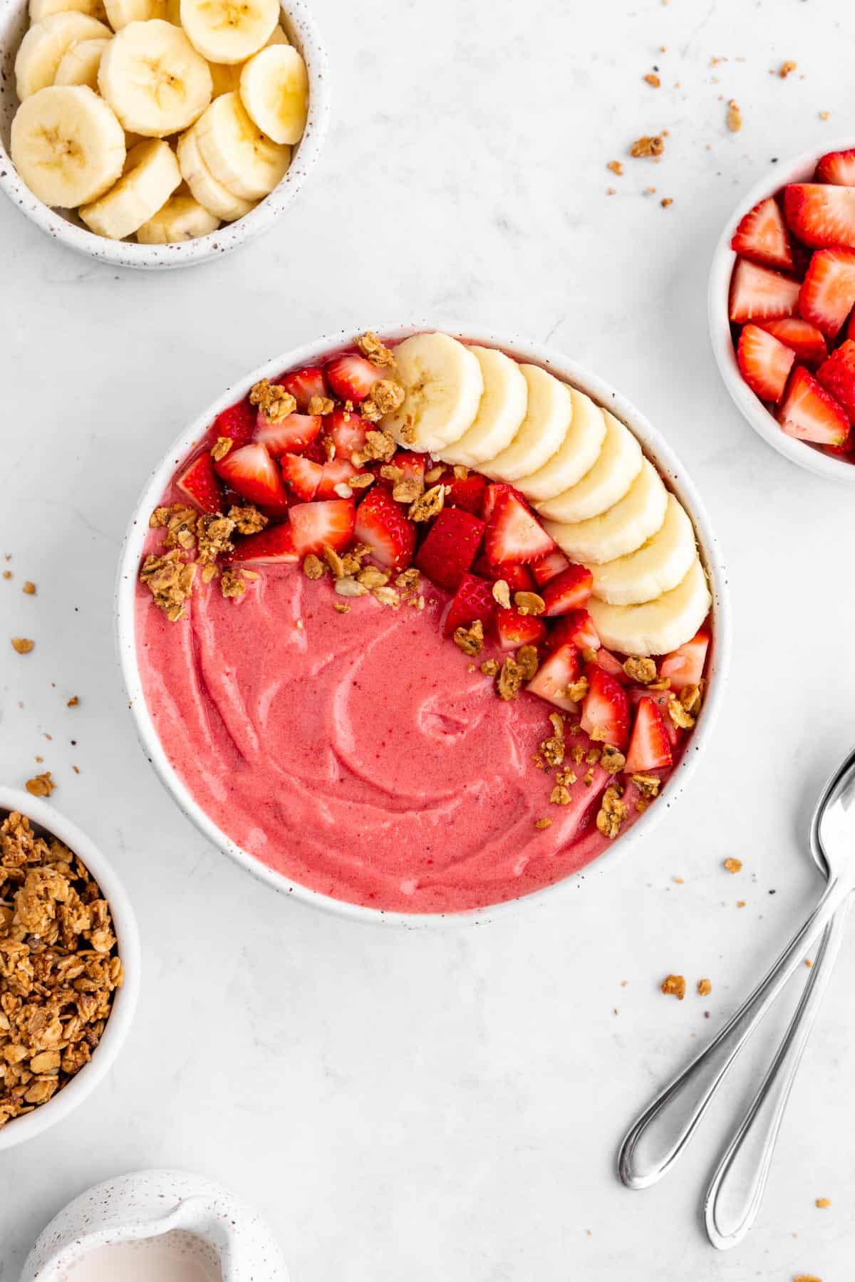 a strawberry banana smoothie bowl surrounded by granola and fresh fruit