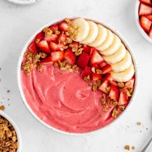 a strawberry banana smoothie bowl surrounded by almond milk, granola, and fresh fruit