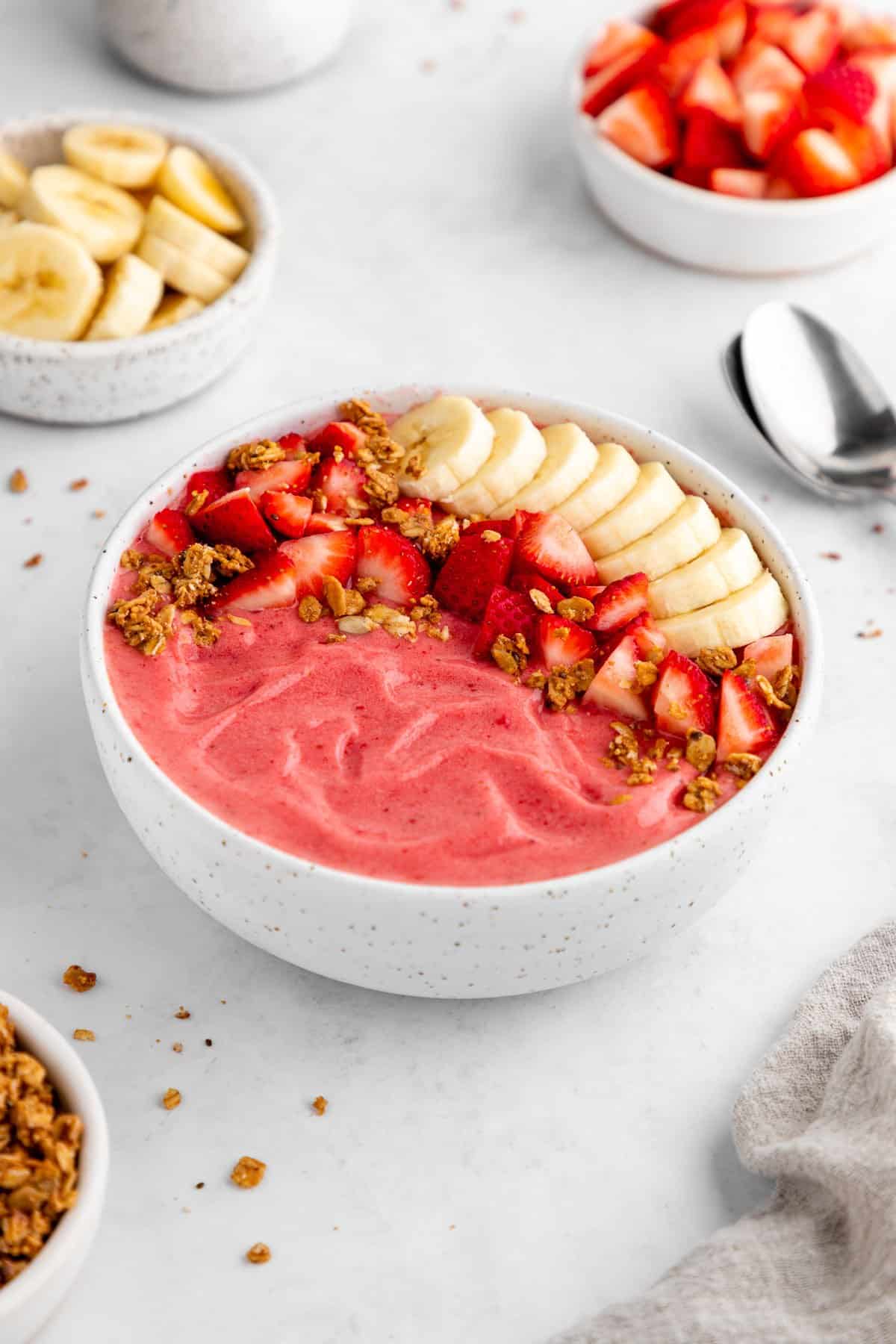 a strawberry banana smoothie bowl with almond milk, granola, and fresh fruit on top