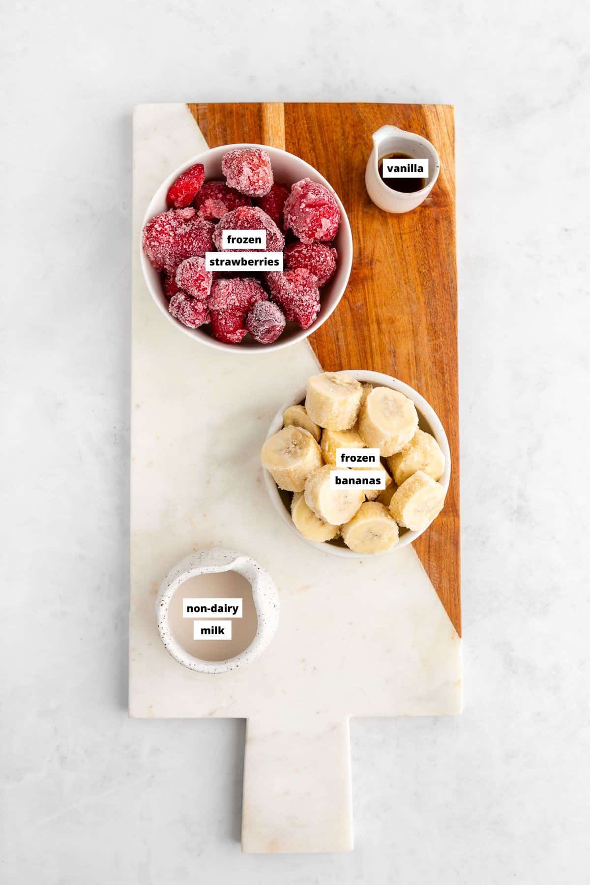 ingredients for a strawberry banana smoothie bowl on a marble board