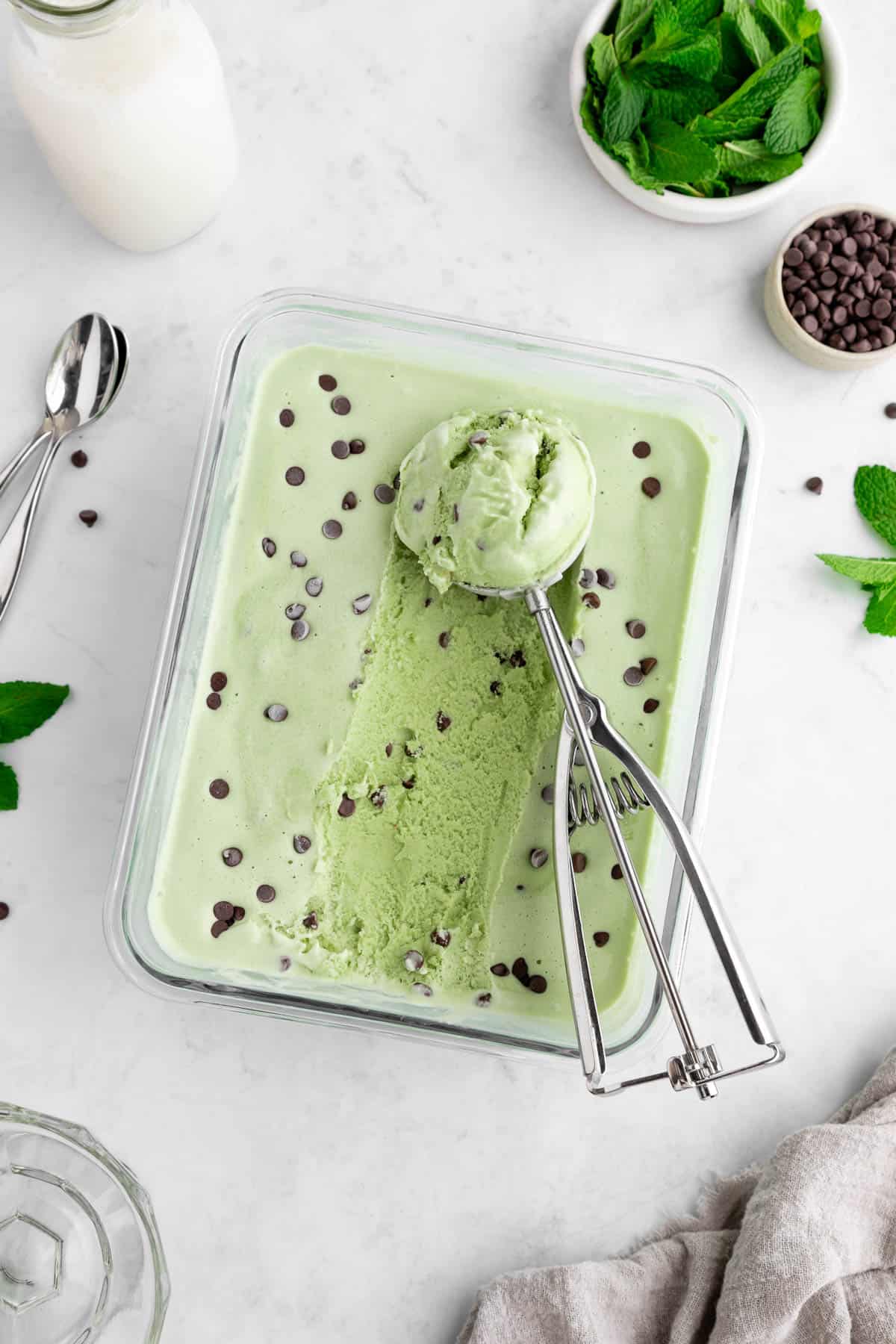 scooping into a glass container of vegan mint chocolate chip ice cream