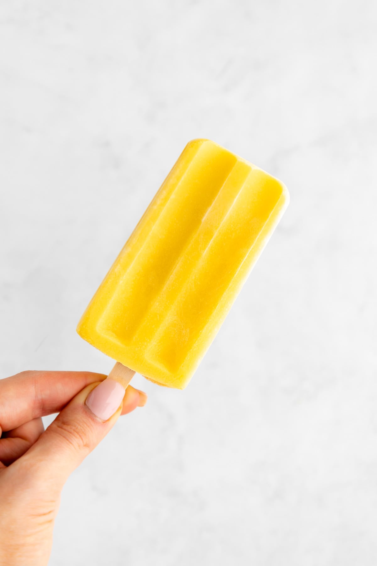 a hand holding a mango lassi popsicle