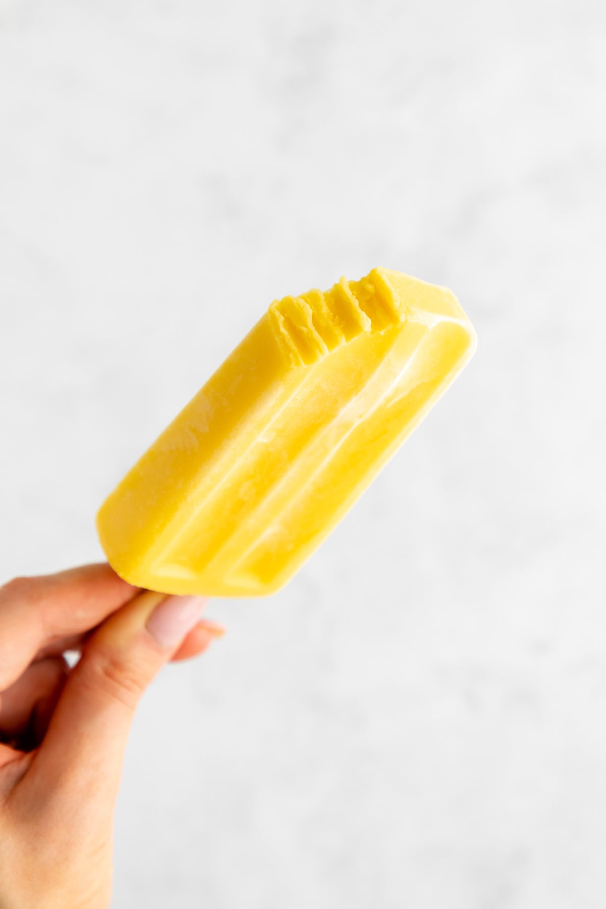 a hand holding a mango lassi popsicle with a bite taken out of it
