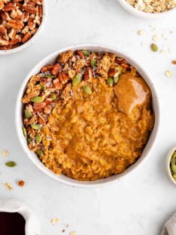 healthy pumpkin oatmeal in a bowl with pecans, almond butter, pumpkin seeds, and maple syrup