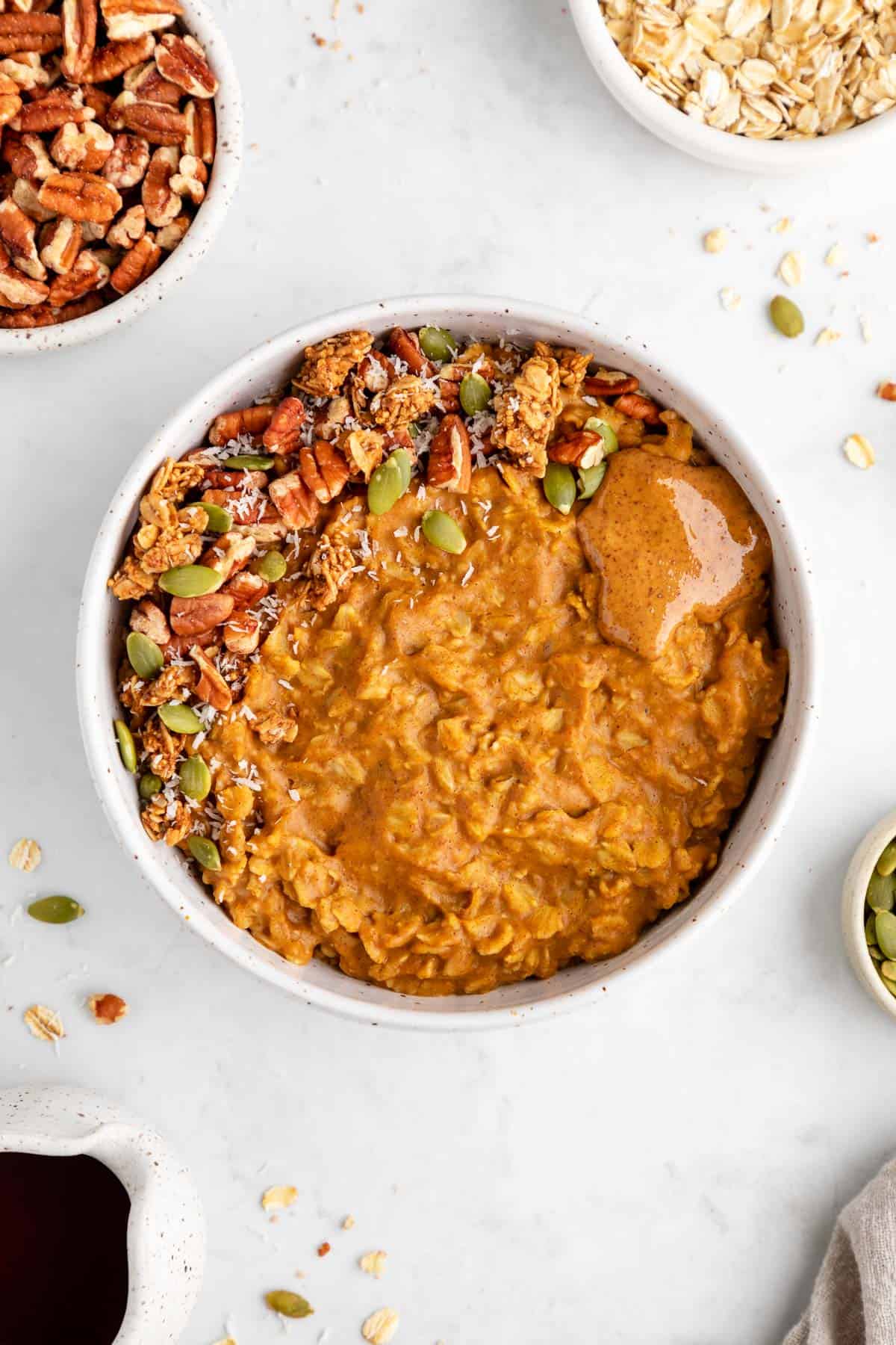 healthy pumpkin oatmeal in a bowl with pecans, almond butter, pumpkin seeds, and maple syrup