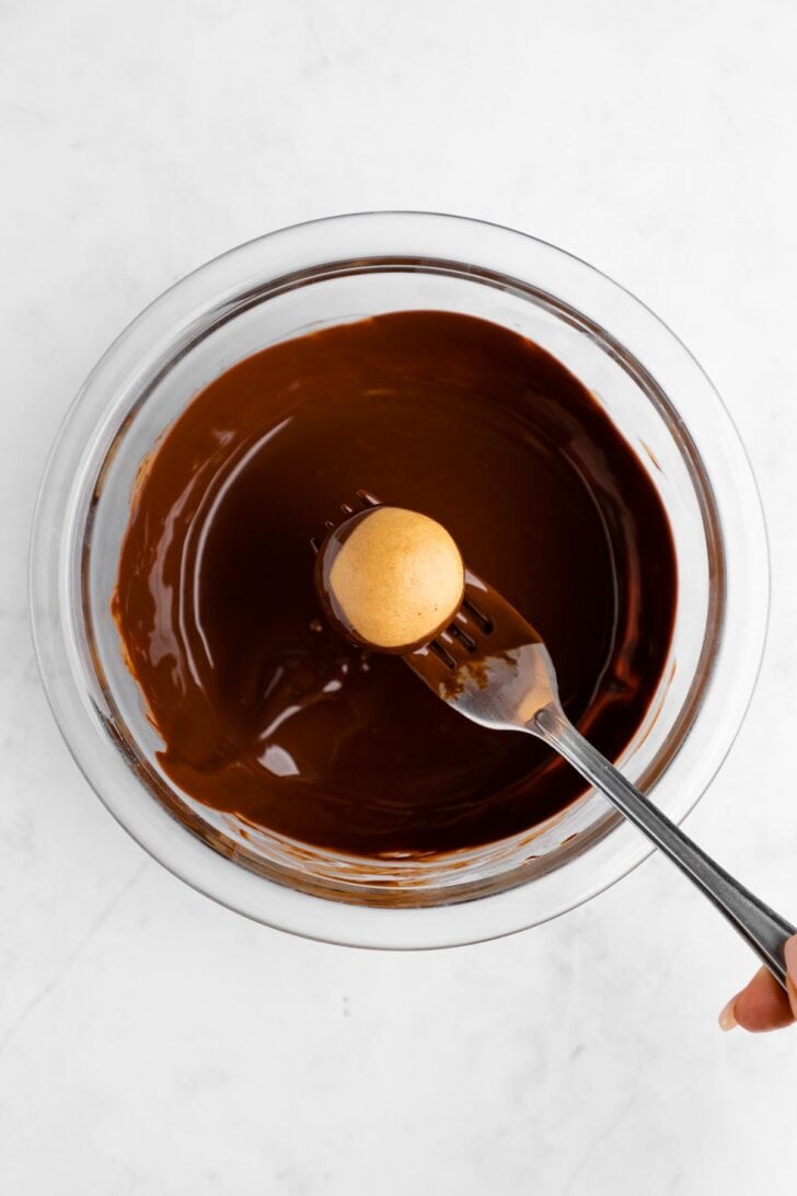 a fork dipping a peanut butter buckeye ball into a bowl of melted chocolate