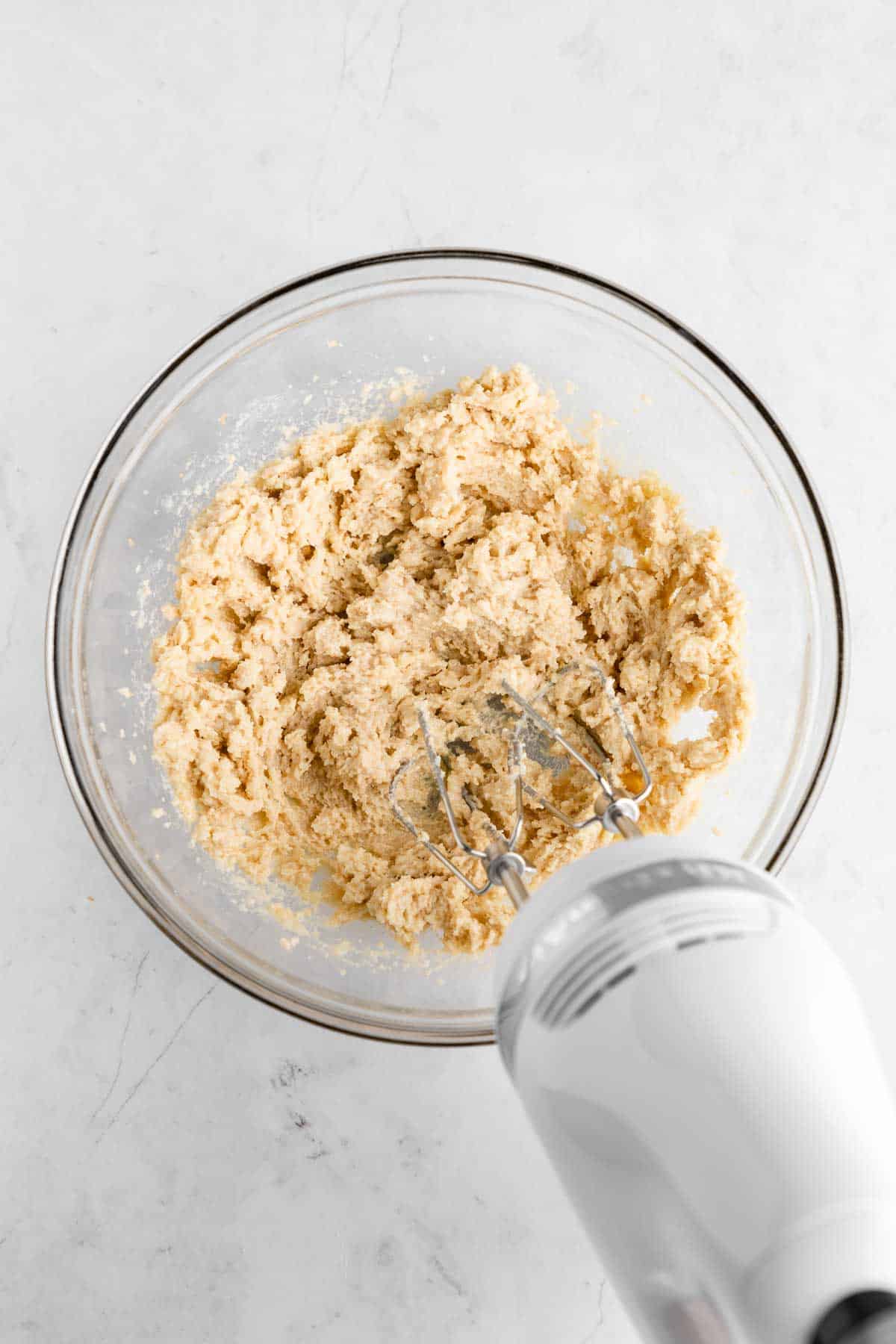 a KitchenAid handheld mixer creaming vegan butter and sugar together in a bowl
