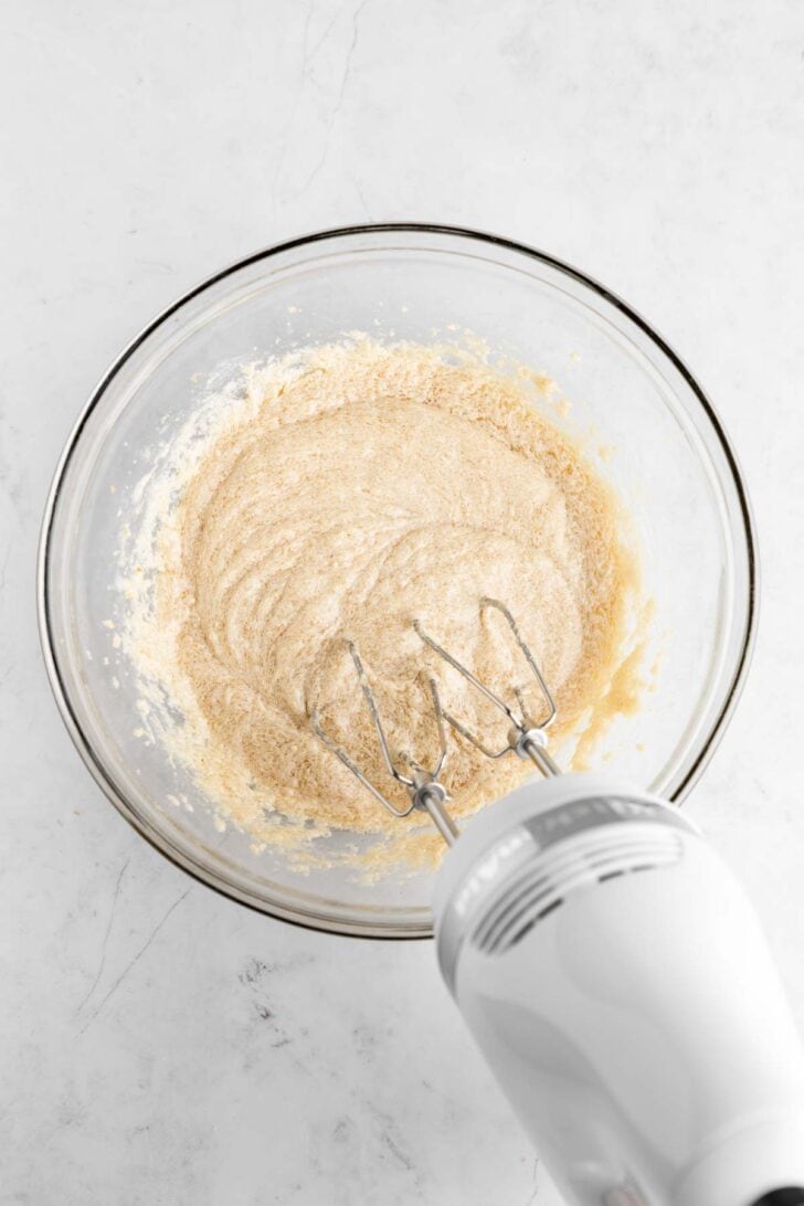 a KitchenAid handheld electric mixer creaming vegan butter, sugar, and almond milk in a glass bowl
